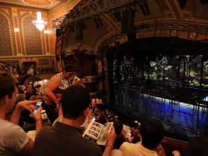 Escena de un musical de Broadway con actores en un escenario iluminado en Nueva York.